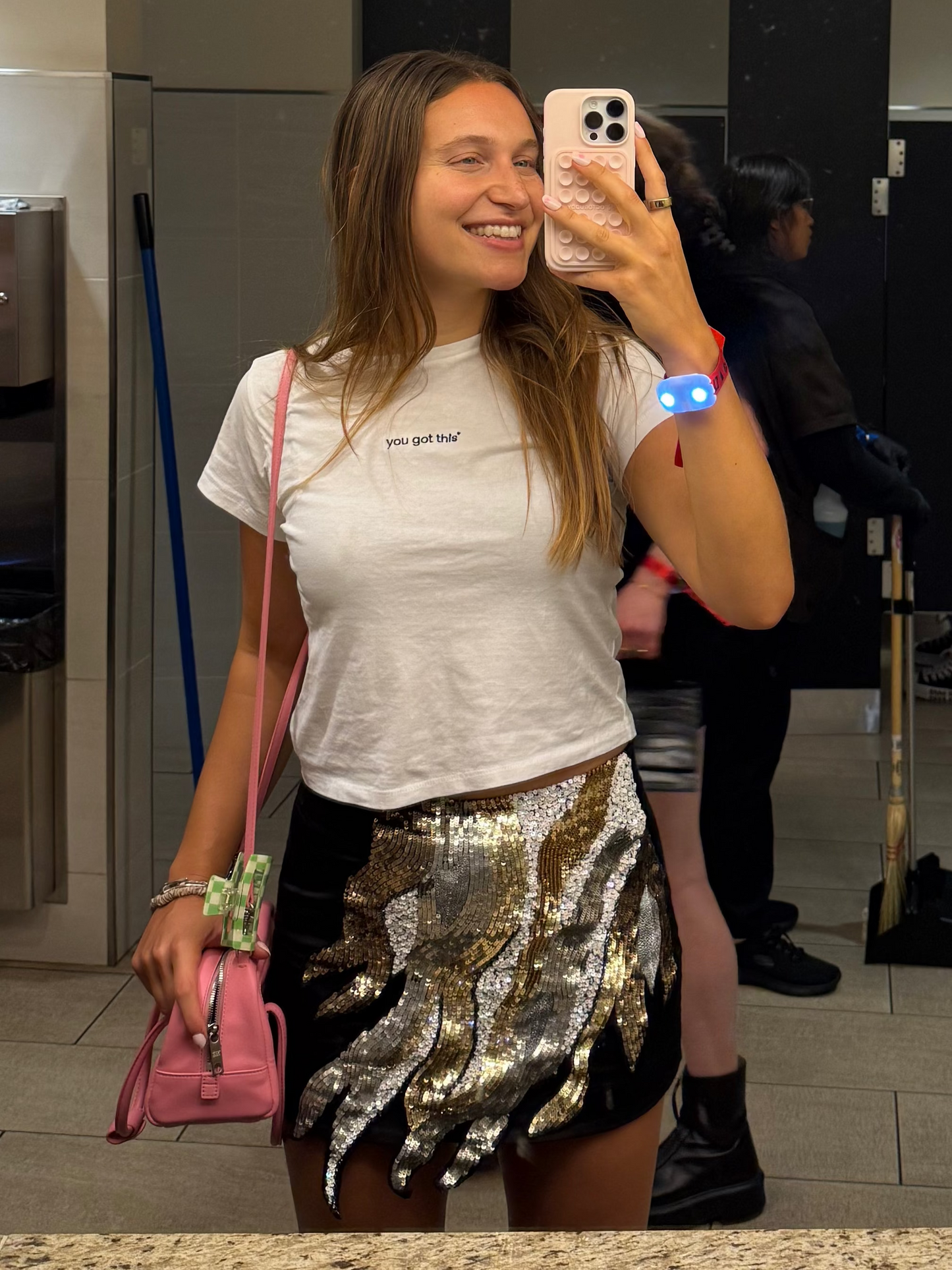 Woman taking a mirror selfie wearing a mirror moments you got this white tee in a public restroom with Gojo soap dispensers.
